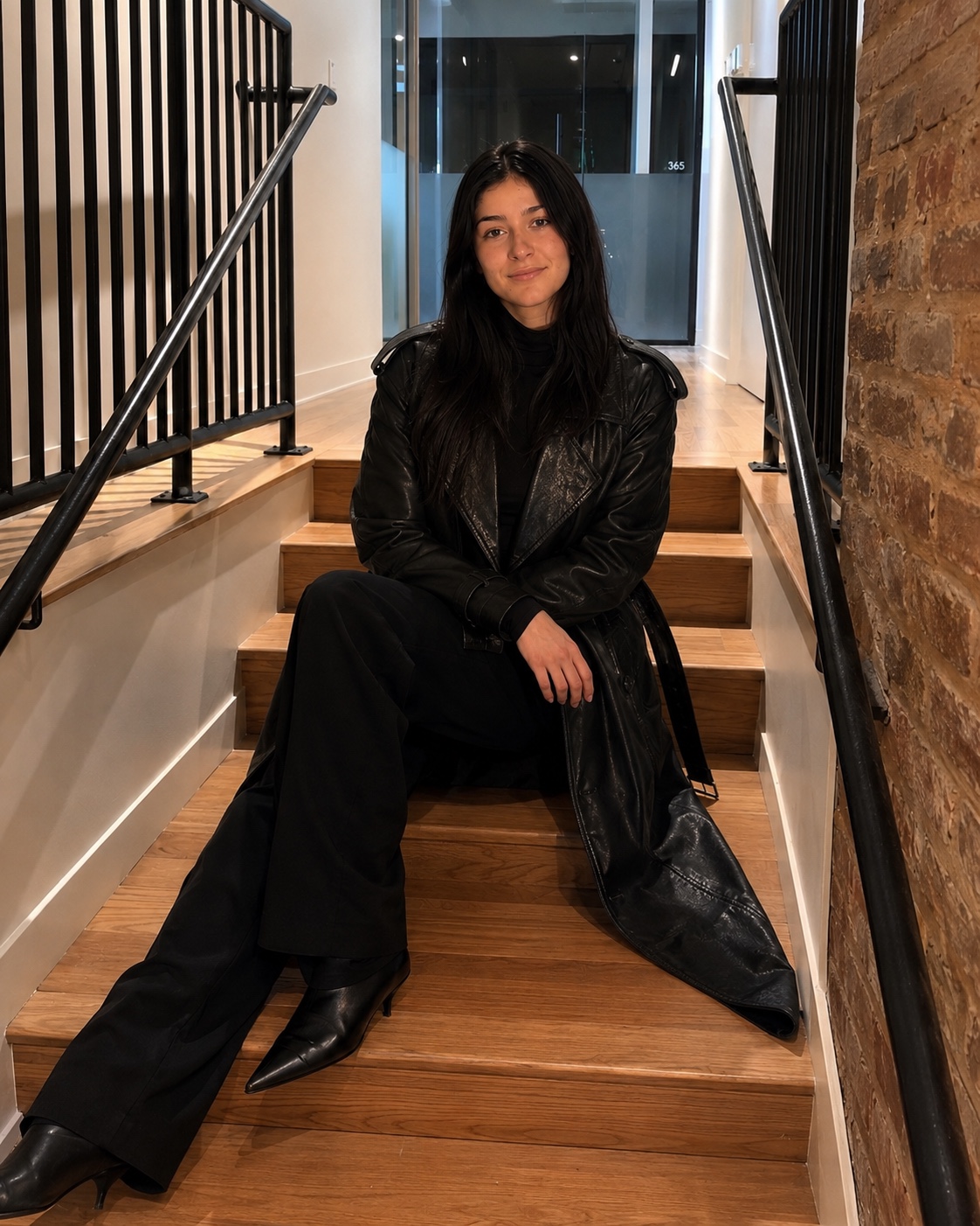 Woman in a black leather coat seated on a wooden staircase
