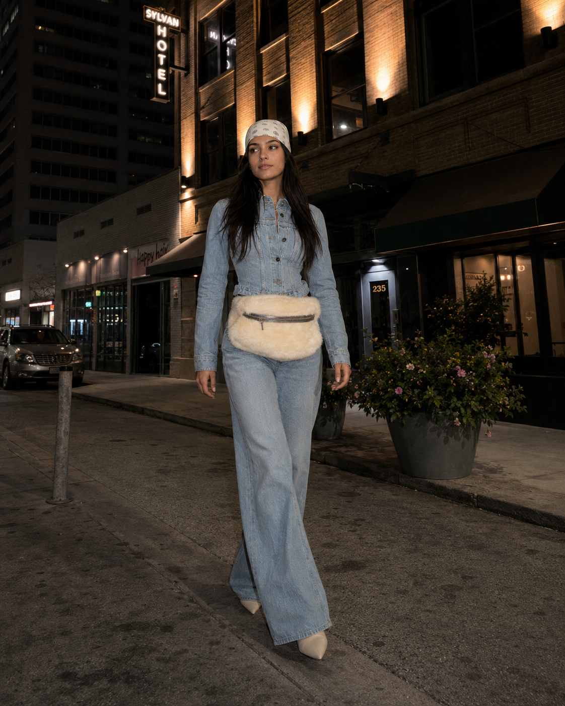 Woman walking at night in a light denim jumpsuit and white fur bag